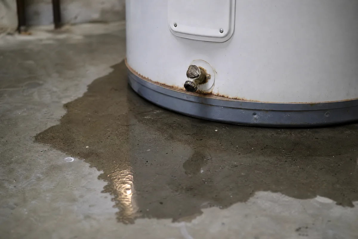 Shallow puddle of water on a basement concrete floor at the corroded base of a residential water heater